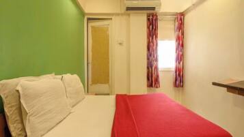 A room with a bed, a green wall, a door, and a window with curtains.