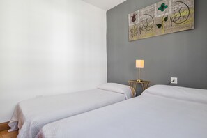 Una habitación con dos camas, una lámpara en la pared y un cuadro.