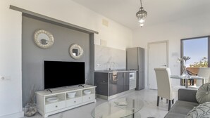 Una cocina moderna con un televisor de pantalla plana, un comedor con mesa de vidrio y un sofá.