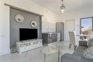 A modern kitchen with a flat-screen TV, a dining area with a glass table, and a sofa.