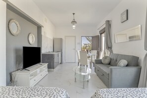 A modern living room with a TV, sofa, dining table, and kitchen area.