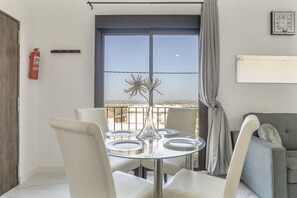 A dining area with a glass table, white chairs, a vase, a fire extinguisher, and a view through a large window.