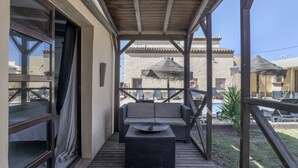 Uma área de estar coberta ao ar livre com um sofá e uma mesa, uma varanda com vista para um edifício com telhado em azulejos e um deck de madeira.