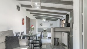 Um interior moderno com sofá, mesa de jantar, cadeiras, cozinha e um quarto com cama e mesas de cabeceira.