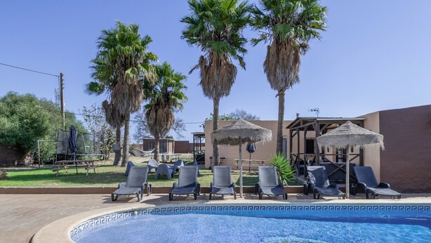 Una piscina con lettini, palme e una zona salotto coperta.