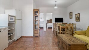 Una cucina con un forno a microonde, un armadietto in legno, un tavolo da pranzo con sedie, un divano giallo e una televisione.