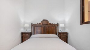 Una camera da letto con una testiera in legno, un letto con copripiumino bianco, due comodini con lampade e uno specchio appeso al muro.