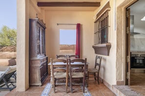 Un coin repas avec une table et des chaises en bois, un buffet et une fenêtre ornée d’un rideau rouge.