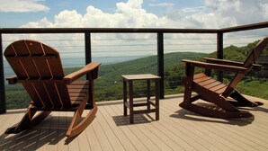 A wooden deck with two rocking chairs and a small table, overlooking a scenic landscape with hills and a body of water. - Ledges   66 with Wintergreen Advantage (Wintergreen)