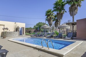 Une piscine avec des chaises longues, des palmiers et un mur en pierre.