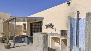 Eine Terrasse mit Steinboden, Sitzgelegenheiten im Freien, einer Steindusche und einem an der Wand befestigten Regal mit Dekoration.