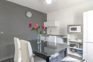 Une cuisine moderne avec une table en verre, des chaises blanches, une horloge et un four à micro-ondes.