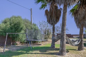 A backyard with a swing set, hammock, palm trees, and a fenced area.