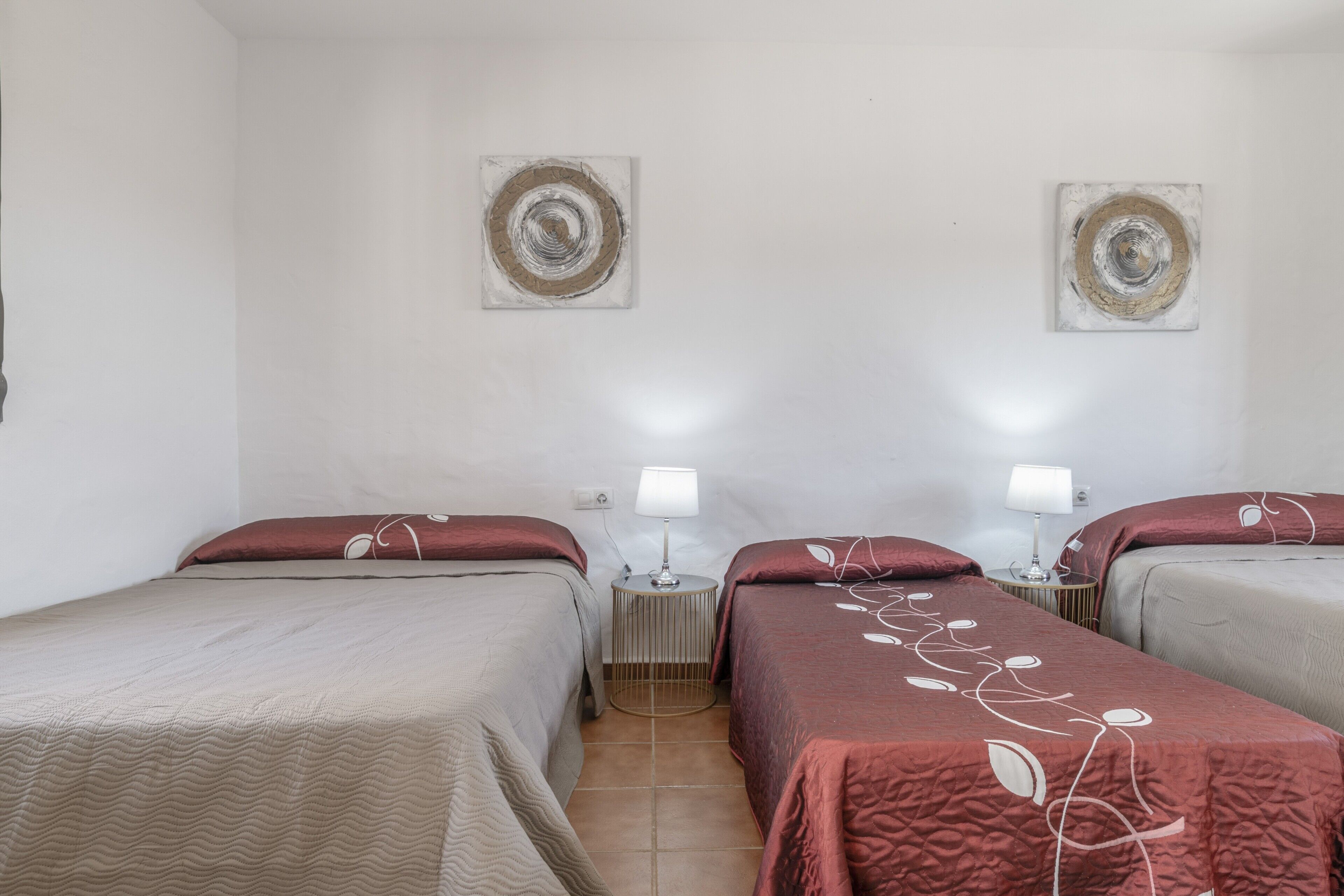 Una habitación de hotel con dos camas, una mesita de noche pequeña con lámpara y dos obras de arte colgadas en la pared.