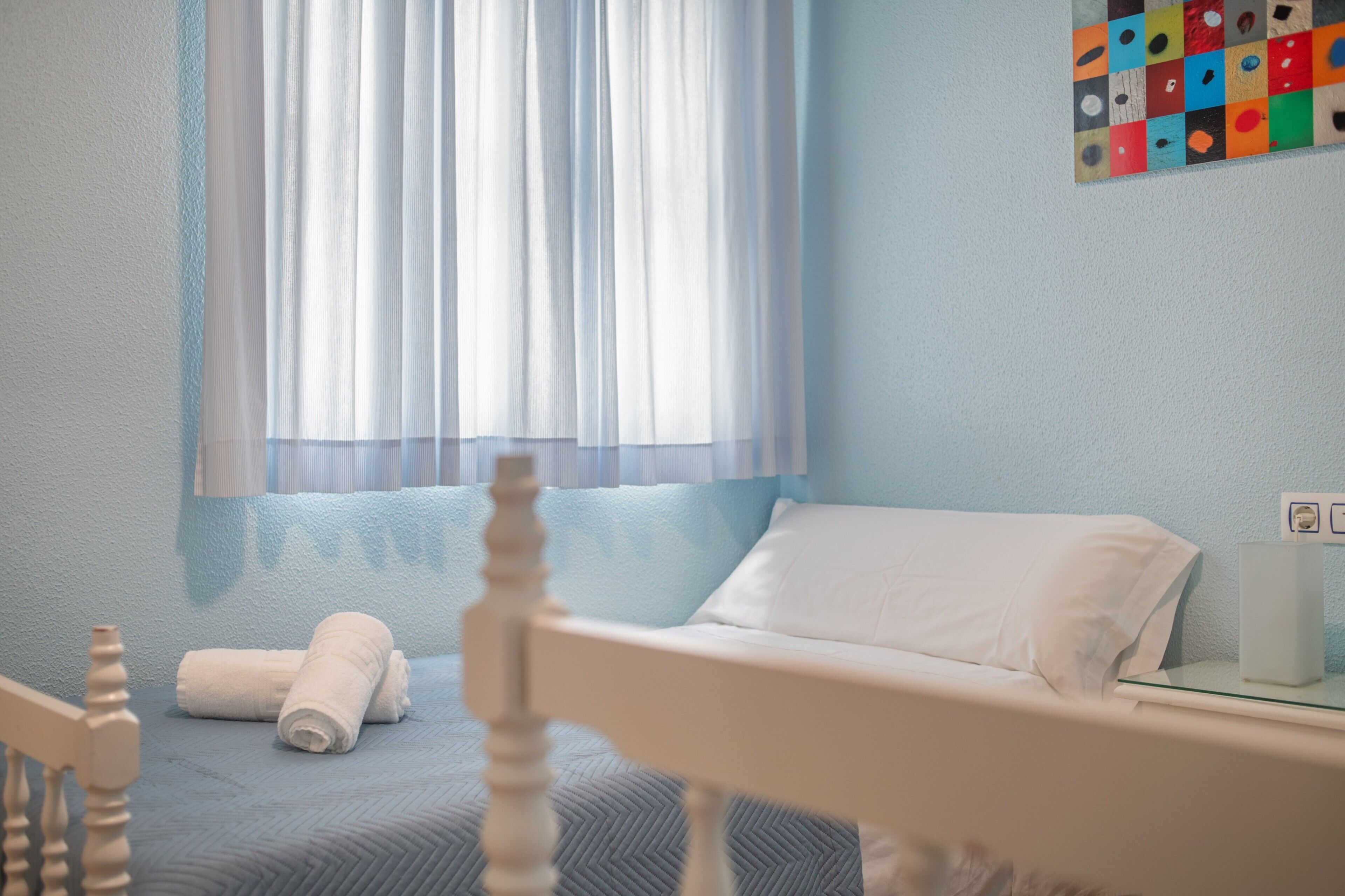 A hotel room with a bed, a chair, a window with sheer curtains, and a wall-mounted artwork.