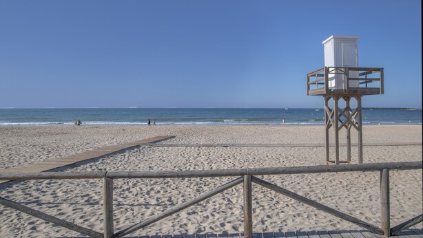 Una playa con una torre de salvavidas, un paseo marítimo de madera y vista al océano.