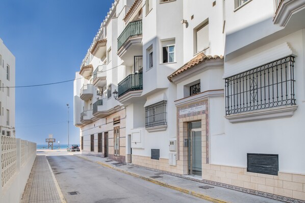Filas de edificios blancos con balcones, cielo despejado y vista distante al mar.