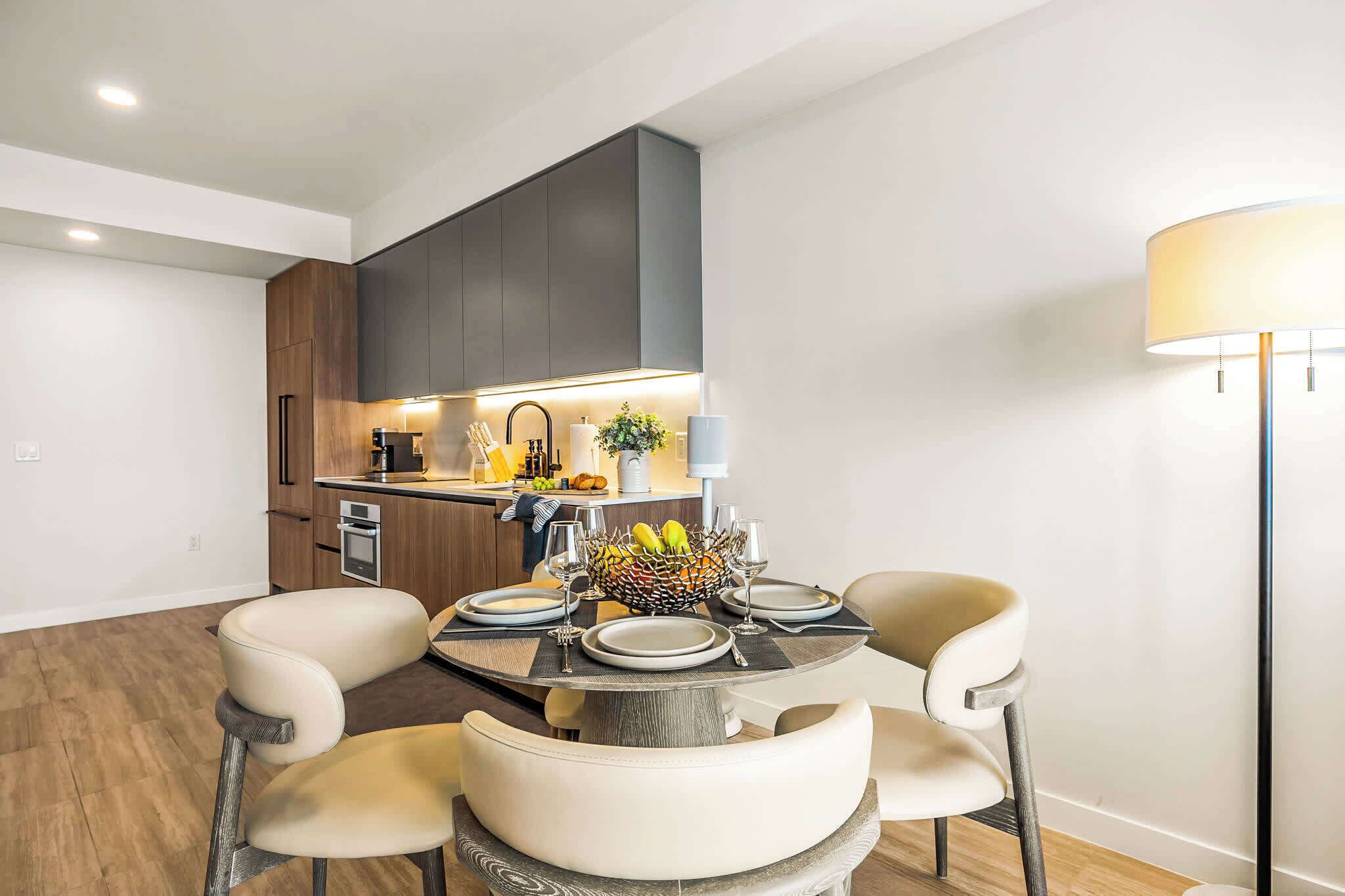 Una cocina moderna con armarios oscuros, una mesa de comedor dispuesta con platos, vasos y un frutero.
