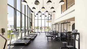 A gym with treadmills, weight machines, and a large window offering a city view.