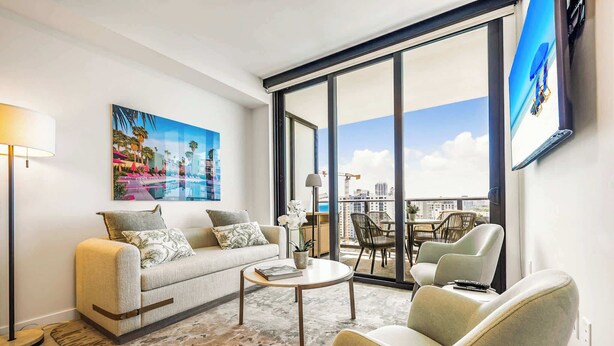 A modern living room with a sofa, armchair, coffee table, and a large window with a view of the city.