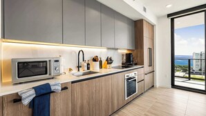 A modern kitchen with a microwave, sink, and oven, wooden cabinets, and a view of the ocean.