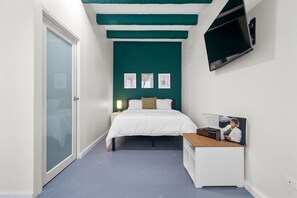 Una habitación pequeña con una cama, un escritorio y un televisor montado en la pared.