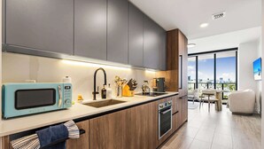 A modern kitchen with a built-in microwave, sink, and oven, wooden cabinets, and a view of the city through large windows.