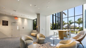 A modern lobby with a seating area, a reception desk, and large windows offering a view of palm trees and buildings.