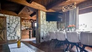 A rustic dining area with stone walls, wooden beams, and a large TV mounted on the wall. - Osada Góralska Ostoja Pod Gubałówką z Jacuzzi (Poronin)