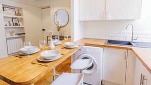A modern kitchen with white cabinetry, a wooden countertop, a built-in washing machine, and a dining area with white chairs and plates. - Quiet Apartment 1br/4p - Place des Victoires (Paris)
