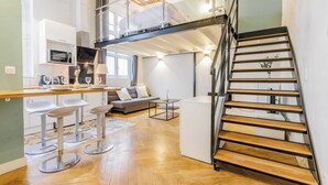 A modern kitchen with a lofted sleeping area, a staircase, and a dining area with bar stools. - Quiet Apartment 1br/4p - Place des Victoires (Paris)