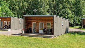 A small cabin with a wooden exterior, a balcony with a table and chairs, and a small garden area. - First Camp Skara - Sommarland (Axvall)
