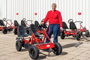 A person standing next to a red three-wheeled vehicle with a steering wheel, in a parking lot with numbered parking spaces. - First Camp Skara - Sommarland (Axvall)