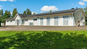 A row of single-room cabins with a central door, each with a small window and a door with a handle. - First Camp Skara - Sommarland (Axvall)