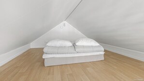 A corner bedroom with a sloped ceiling, a bed with white bedding, and a wooden floor. - First Camp Skara - Sommarland (Axvall)