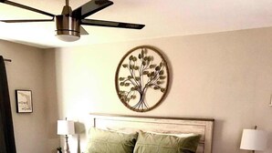 A bedroom with a wooden bed, a ceiling fan, a wall-mounted tree decoration, and a nightstand with a lamp. - Quiet 3BR retreat - pool, gym & Disney close (Kissimmee)