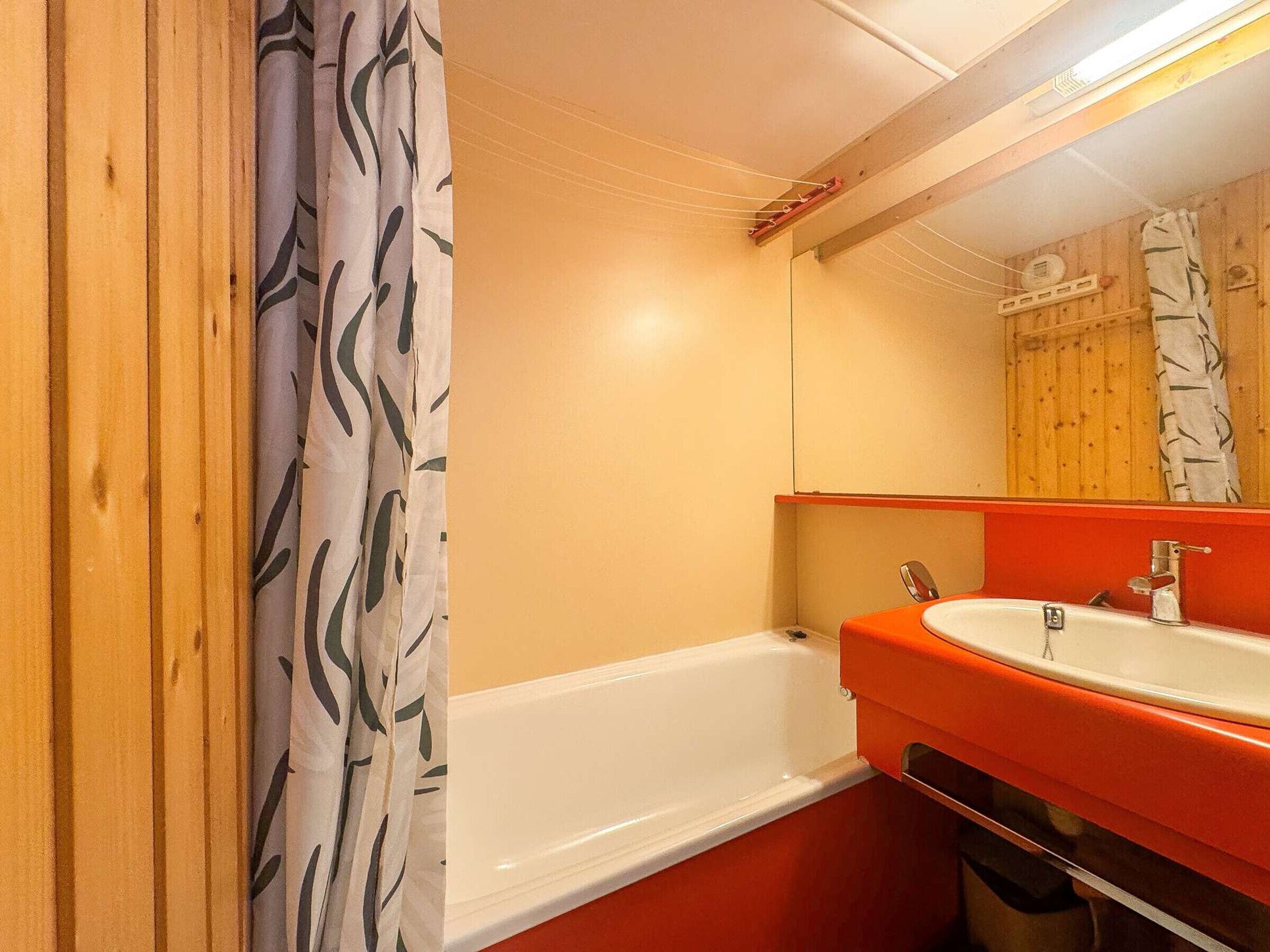 Ein Badezimmer mit einer weißen Badewanne, einem orangefarbenen Waschbecken und einem Spiegel darüber.