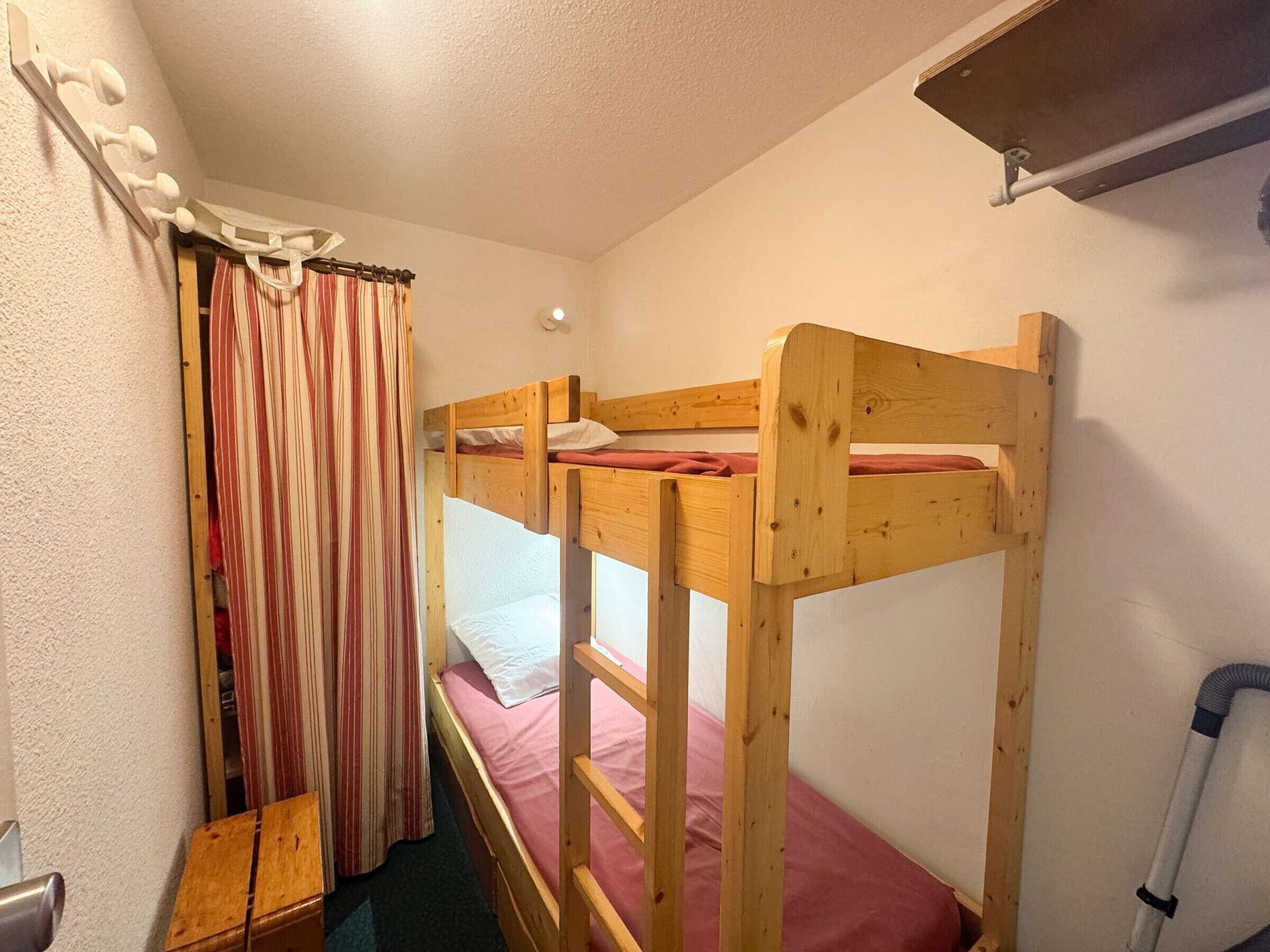 A bunk bed room with a wooden headboard, a striped curtain, and a small wooden bench.