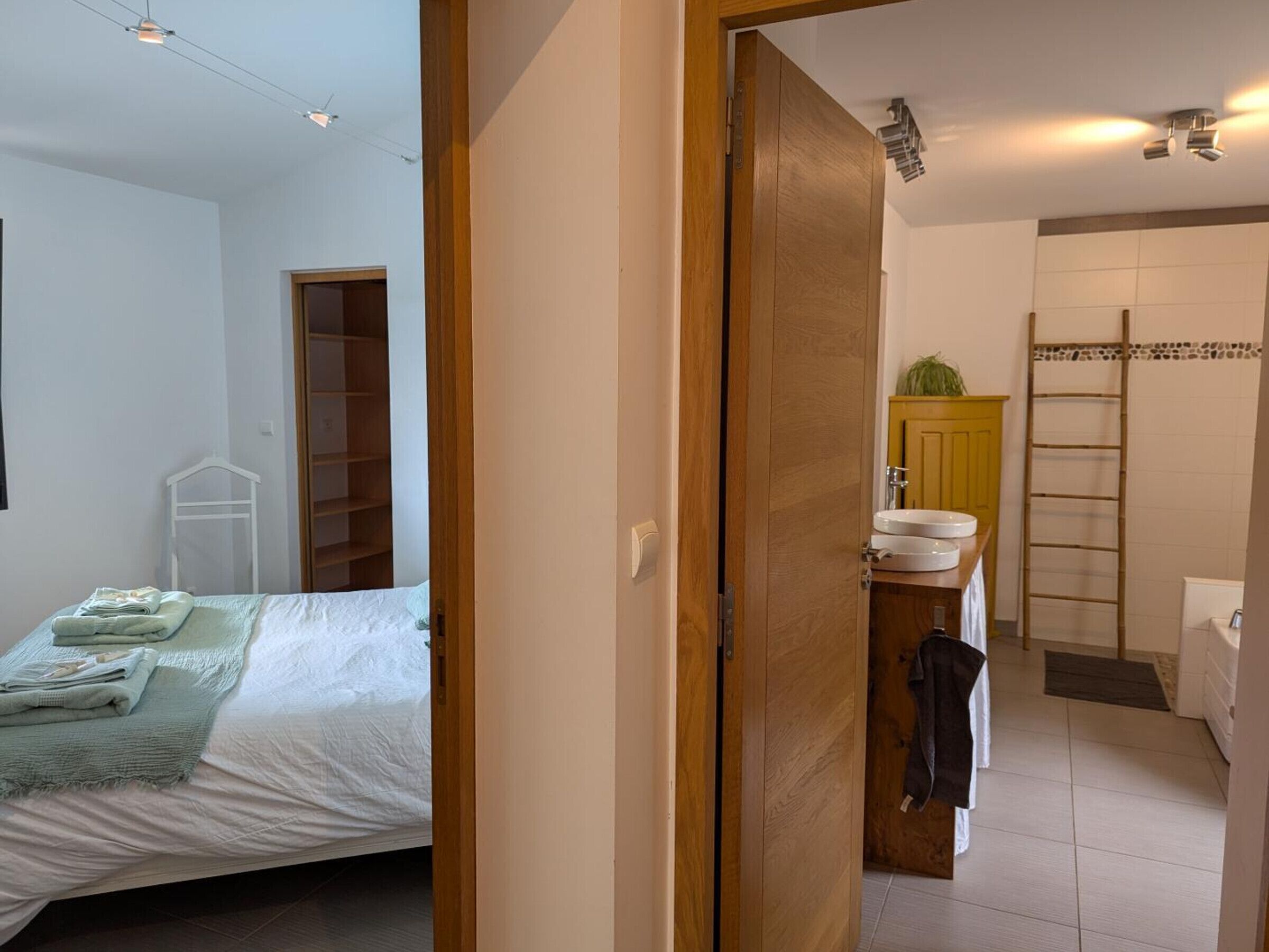 Ein Schlafzimmer mit einem Bett, einem Holzschrank und einem Badezimmer mit Waschbecken und Handtuchhalter.