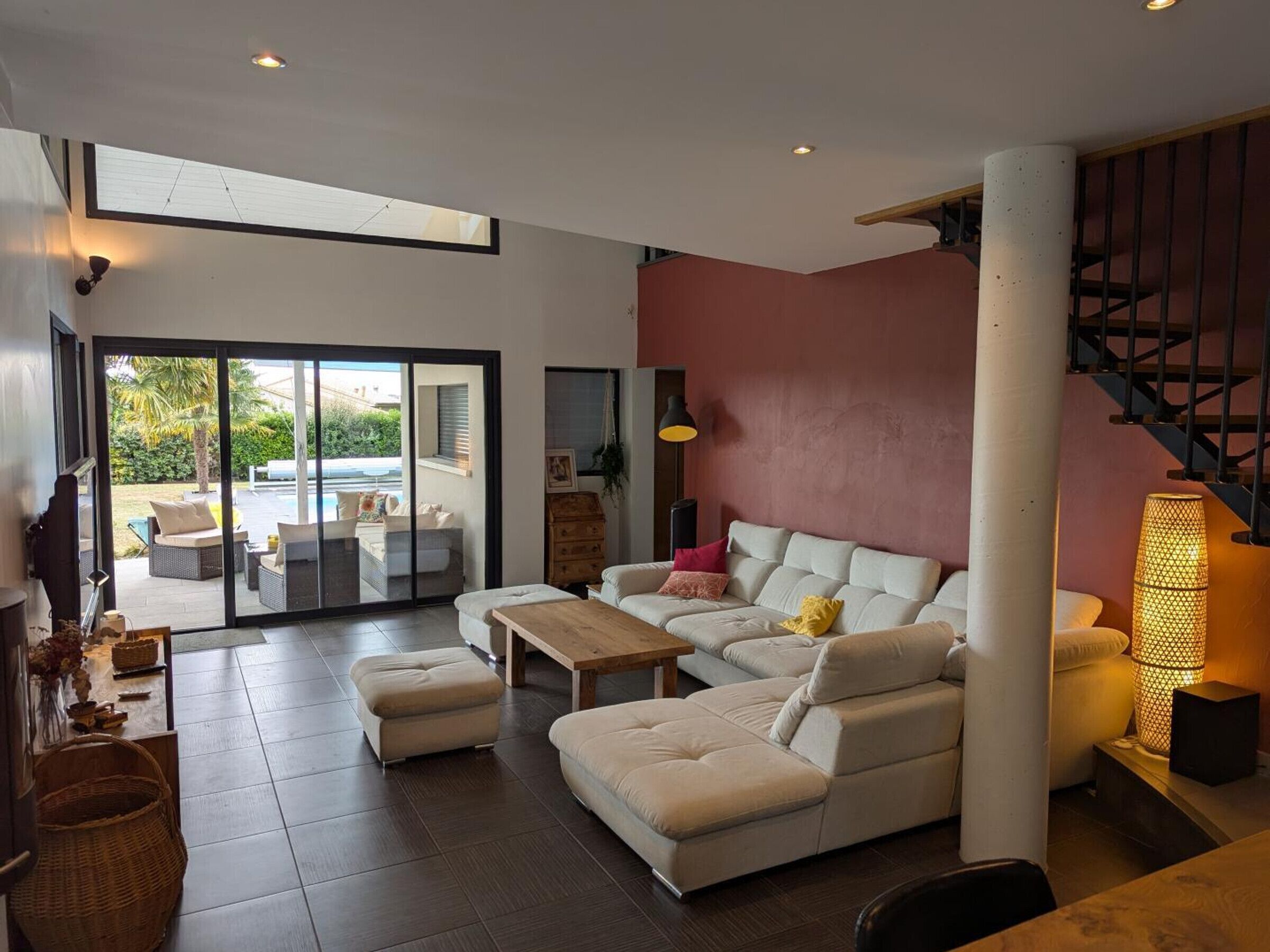 Ein modernes Wohnzimmer mit einer Sofagarnitur, einem Couchtisch und einem Kamin. Eine Schiebetür aus Glas führt zu einem Außenbereich mit einem Pool.
