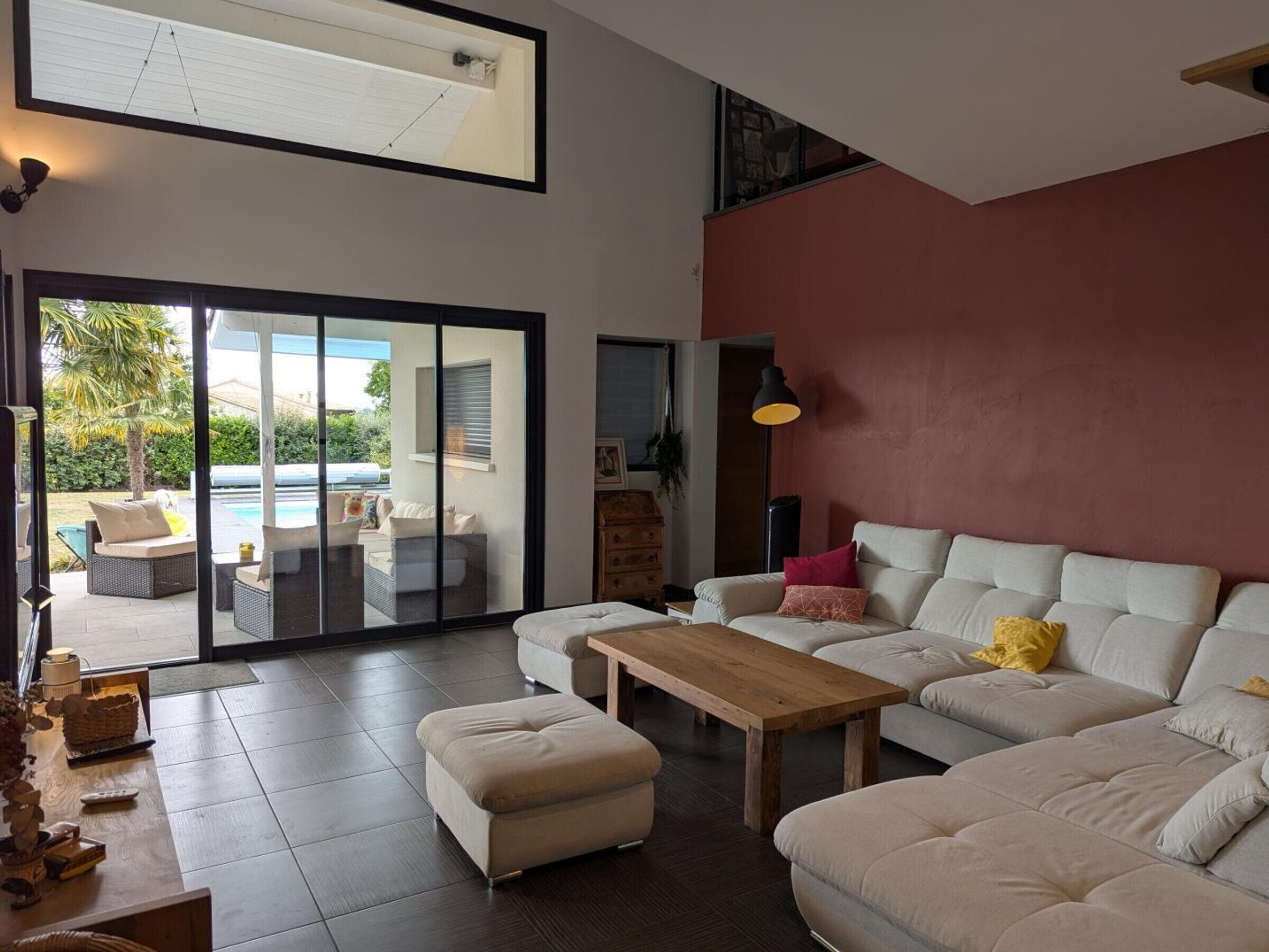 A spacious living area with a large sofa, a wooden coffee table, and a sliding glass door leading to an outdoor patio with a pool.