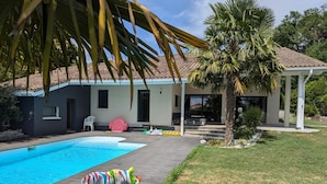A swimming pool with a wooden deck, a small building with a tiled roof, and a palm tree.