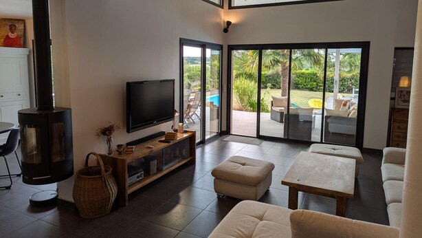 A modern living room with a fireplace, a flat-screen TV, and a large sliding glass door leading to an outdoor patio with a pool and furniture.