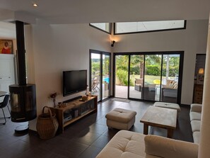 Una sala de estar moderna con chimenea, televisor de pantalla plana y un gran ventanal corredero que da a un patio exterior con piscina y mobiliario.