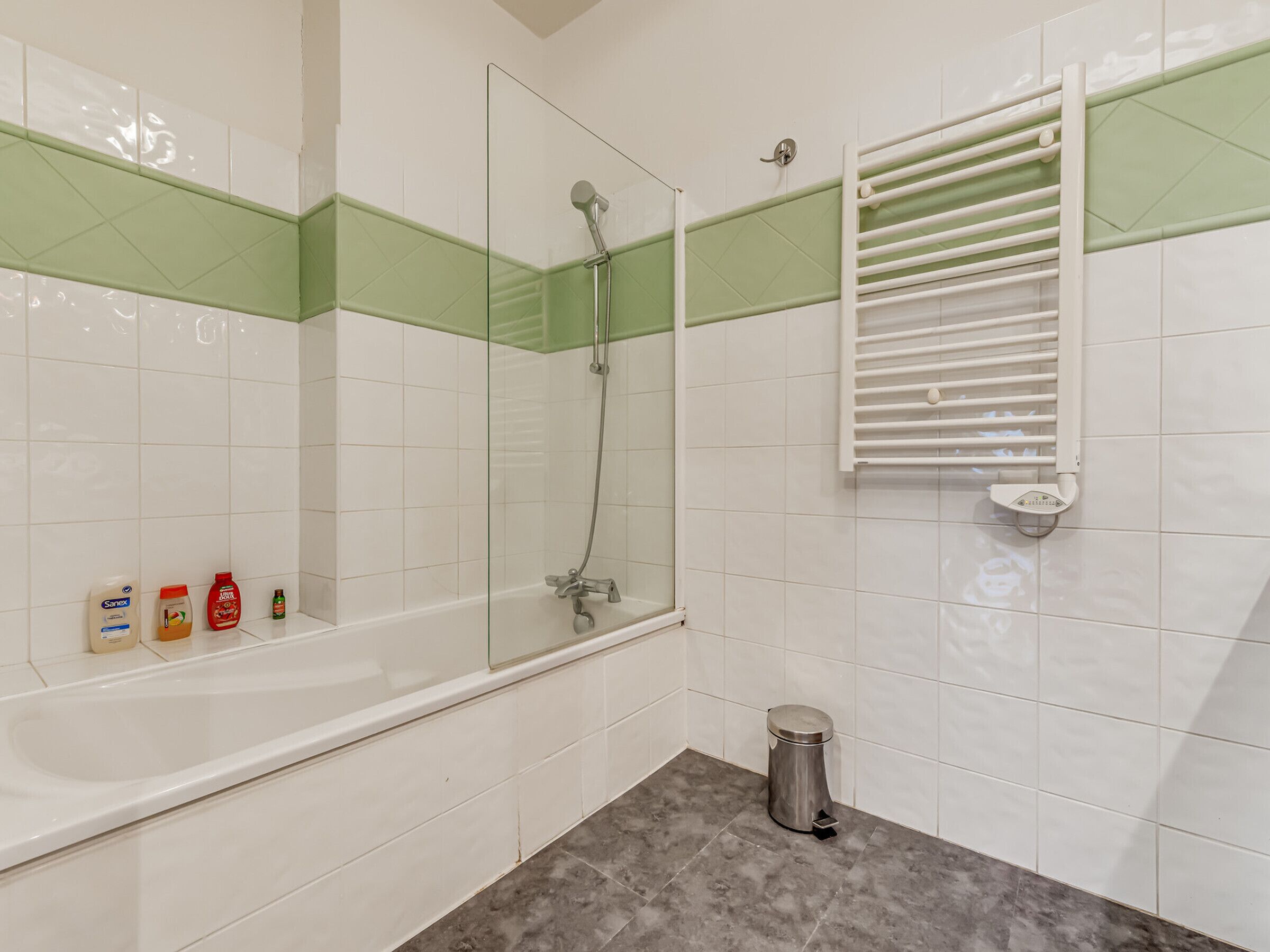 Un baño con bañera, ducha y retrete. Hay artículos de aseo en la encimera.