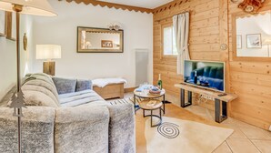 Ein gemütliches Zimmer mit Holzvertäfelung, einer Couch, einem Fernseher und einem kleinen Tisch mit einer Flasche und Gläsern.