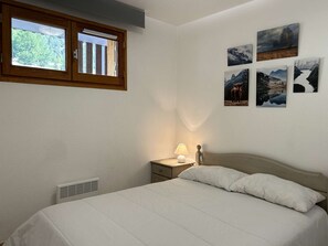 A bedroom with a bed, a nightstand, a lamp, and a window with blinds. - Ski Apartment in Montgenèvre, 4 pax, parking included (Montgenèvre)