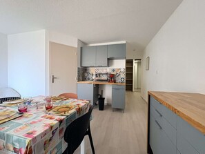 Uma cozinha compacta com área de jantar, com uma mesa adornada por um guardanapo floral, uma cadeira preta e bancada com pia e cafeteira.