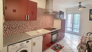 Una cocina con gabinetes rojos, salpicadero de azulejos, lavadora, horno y ventilador de techo.