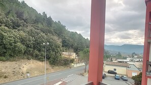 Un balcón con vistas a una carretera, una ladera boscosa y una cadena montañosa distante.